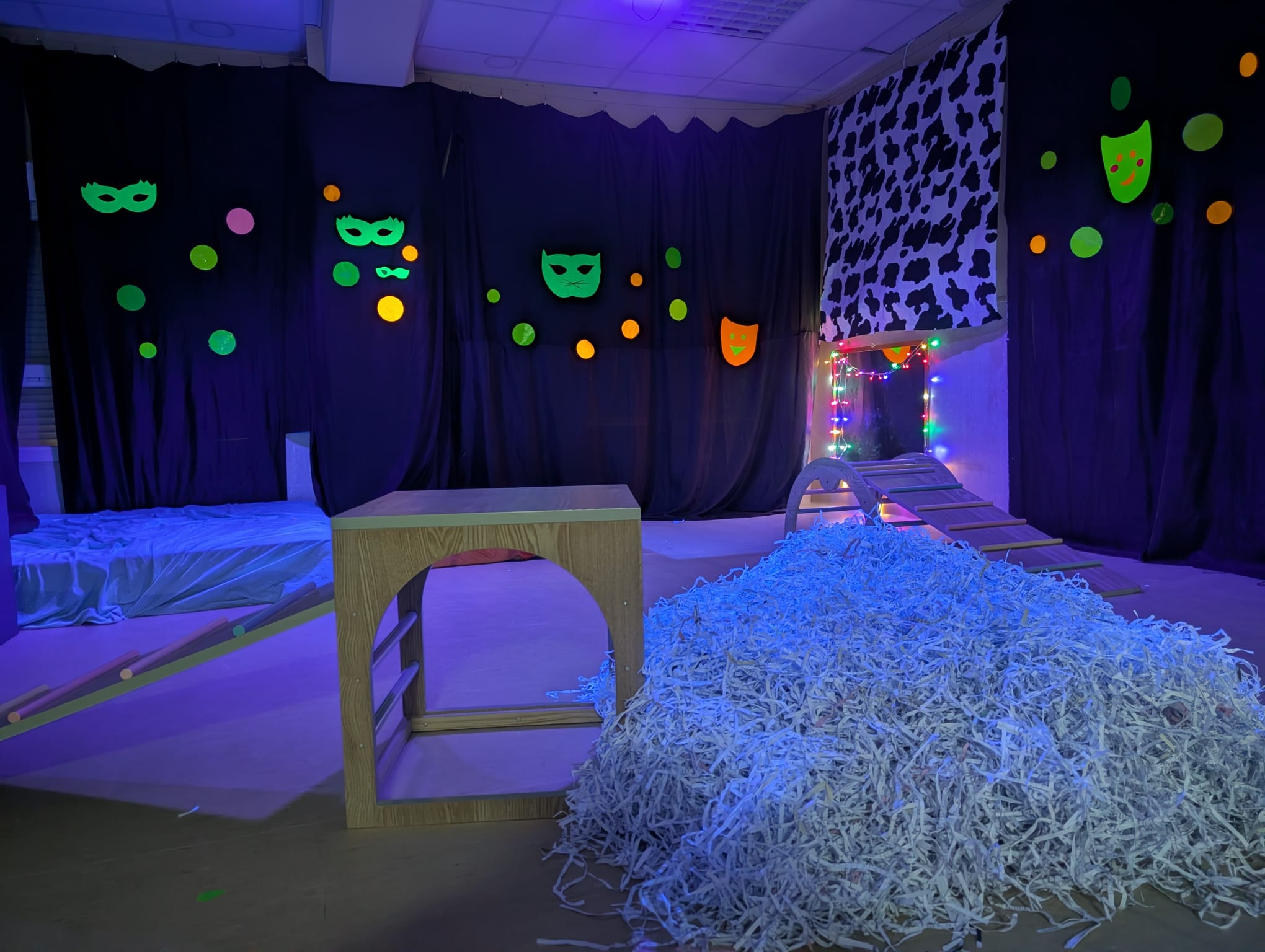 Primer plano de una montaña de papel triturado blanco junto a un cubo de madera en una sala con iluminación ultravioleta.